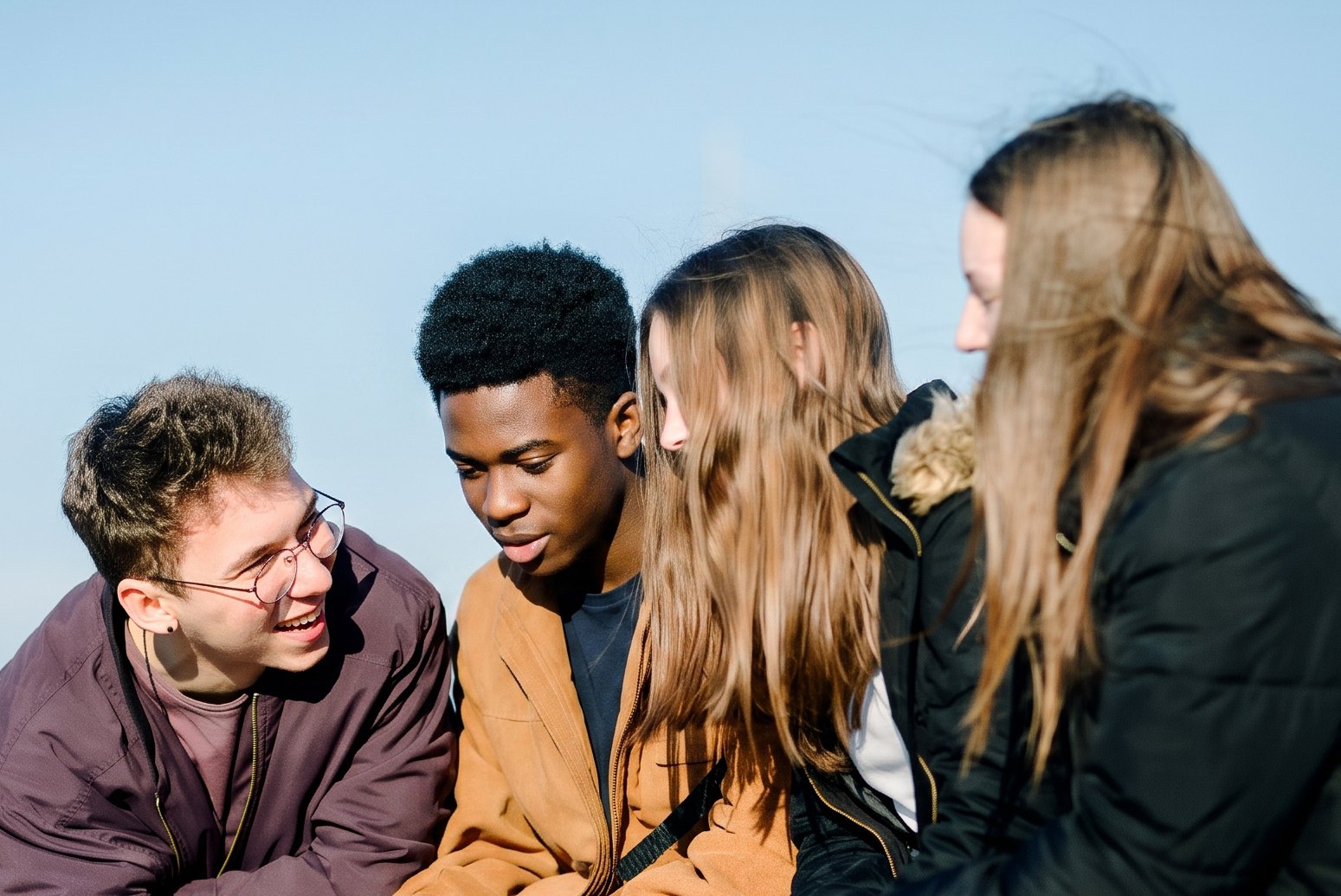 Vier junge Menschen sitzen nebeneinander im Freien und unterhalten sich