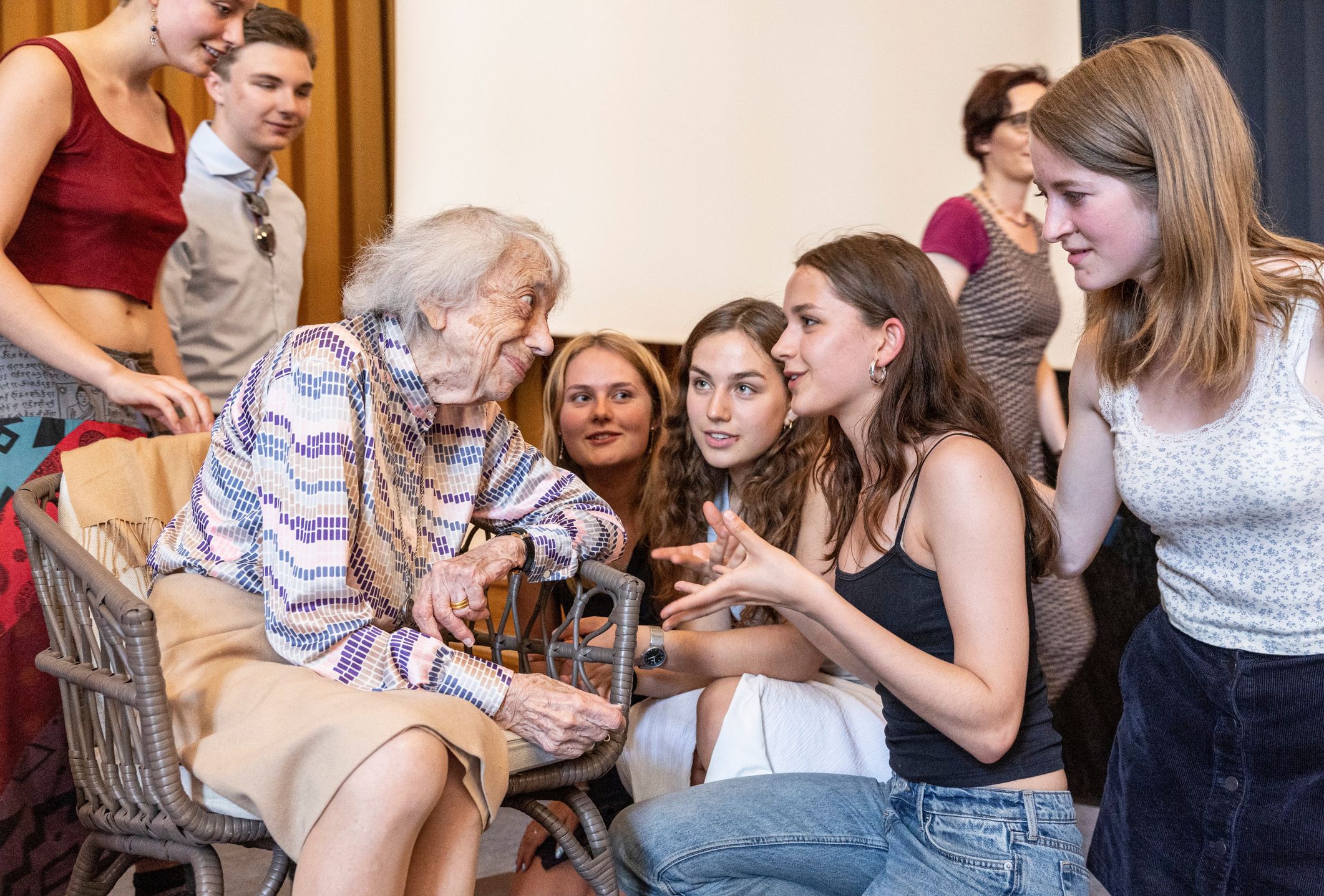 Margot Friedländer sitzt in einem Sessel und spricht mit jungen Menschen, die sich zu ihr hinunterbeugen